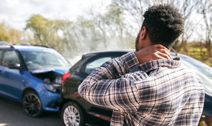 Man holding his neck in pain at the scene of a rear-end car accident, illustrating the common injury and the need for medical care and legal action by a personal injury lawyer.